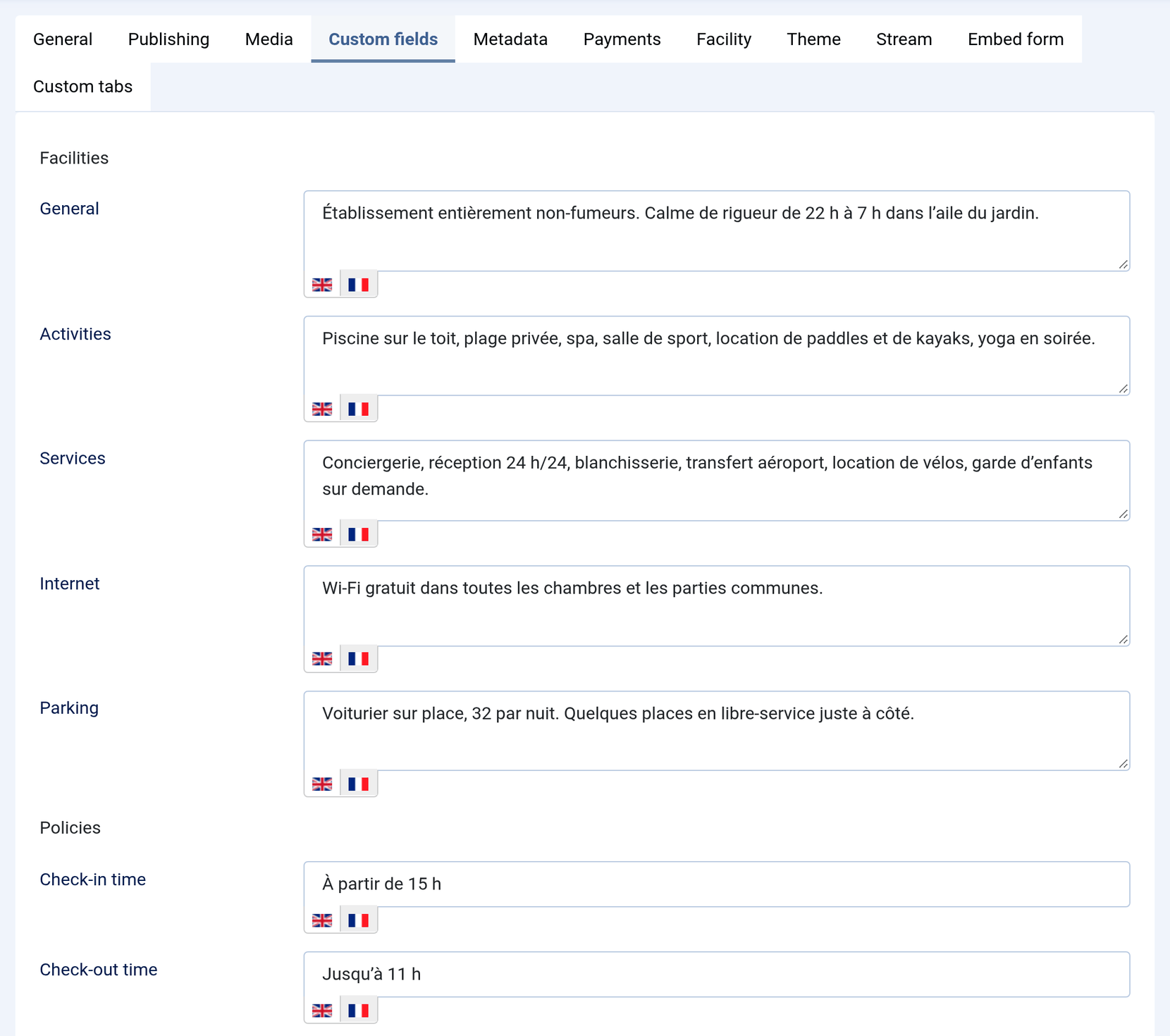 The Custom fields tab of a property with its French tabs open: Facilities (General, Activities, Services, Internet, Parking) and Policies (Check-in time À partir de 15 h, Check-out time Jusqu’à 11 h), each with an English and a French flag.